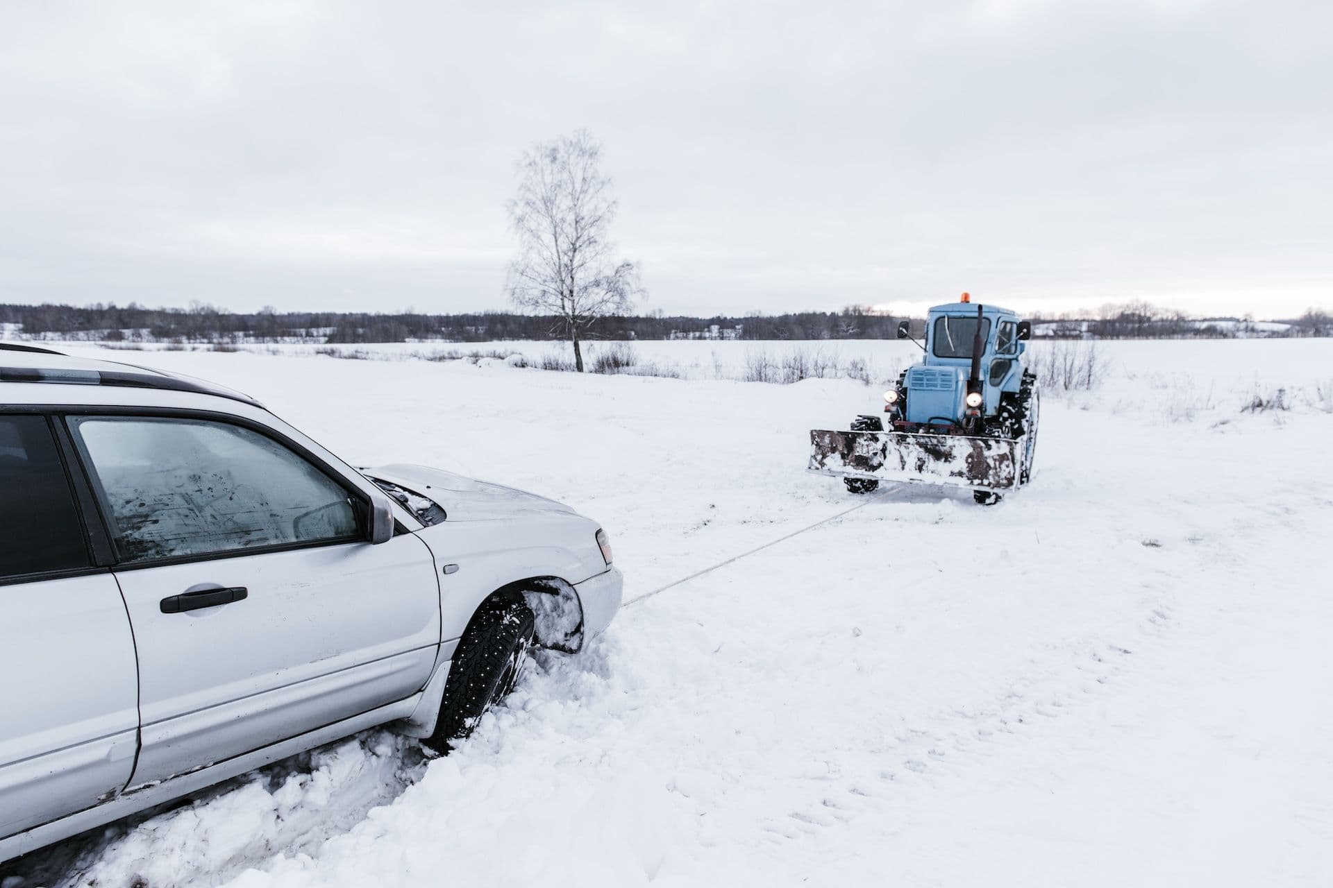 A tractor towing a car over a snow field after a snow accident.