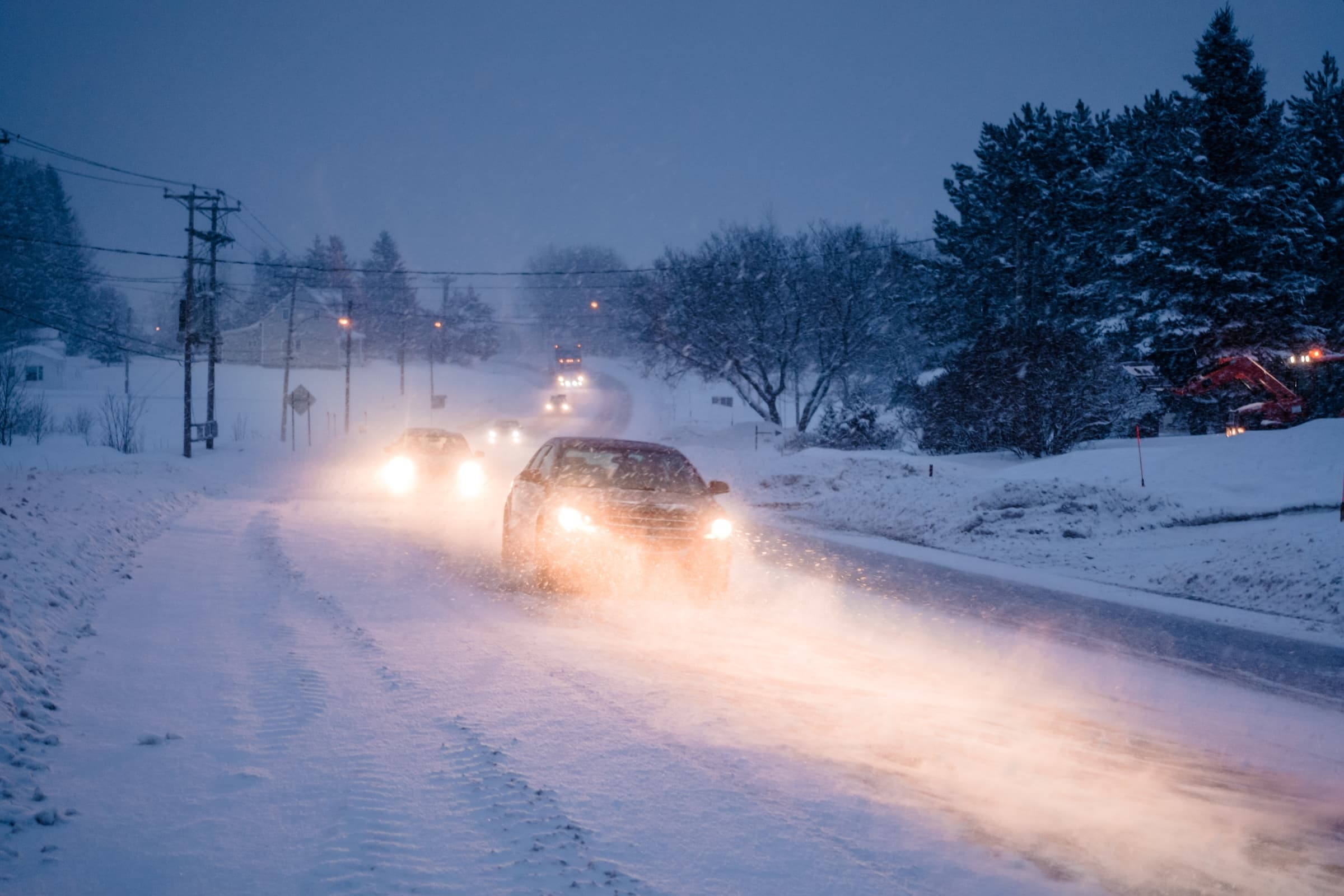 A line of cars in snowy weather using low-beam headlights to navigate hazardous winter driving conditions in Oregon.