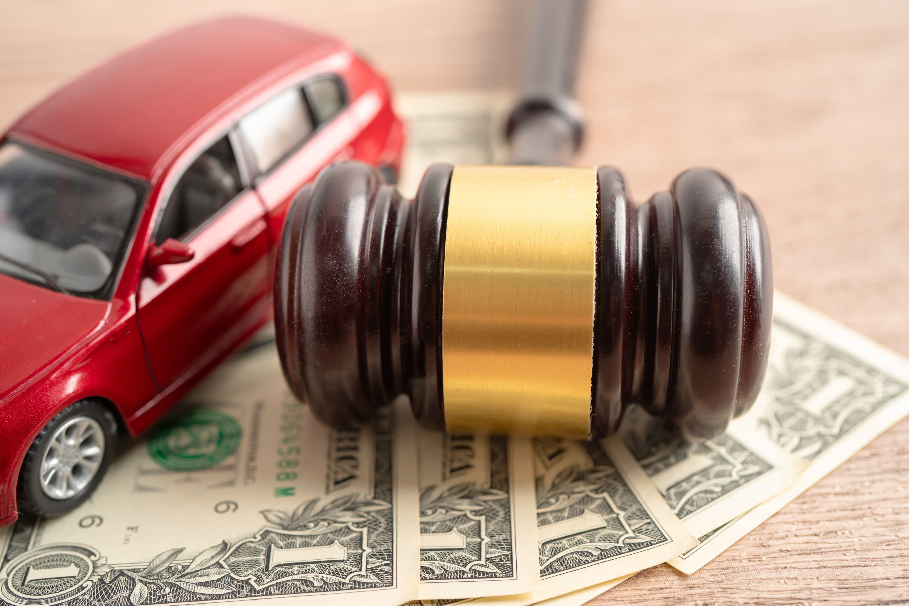 A toy car and a gavel on top of fanned out dollar bills, illustrating the potential for car crash injury compensation.