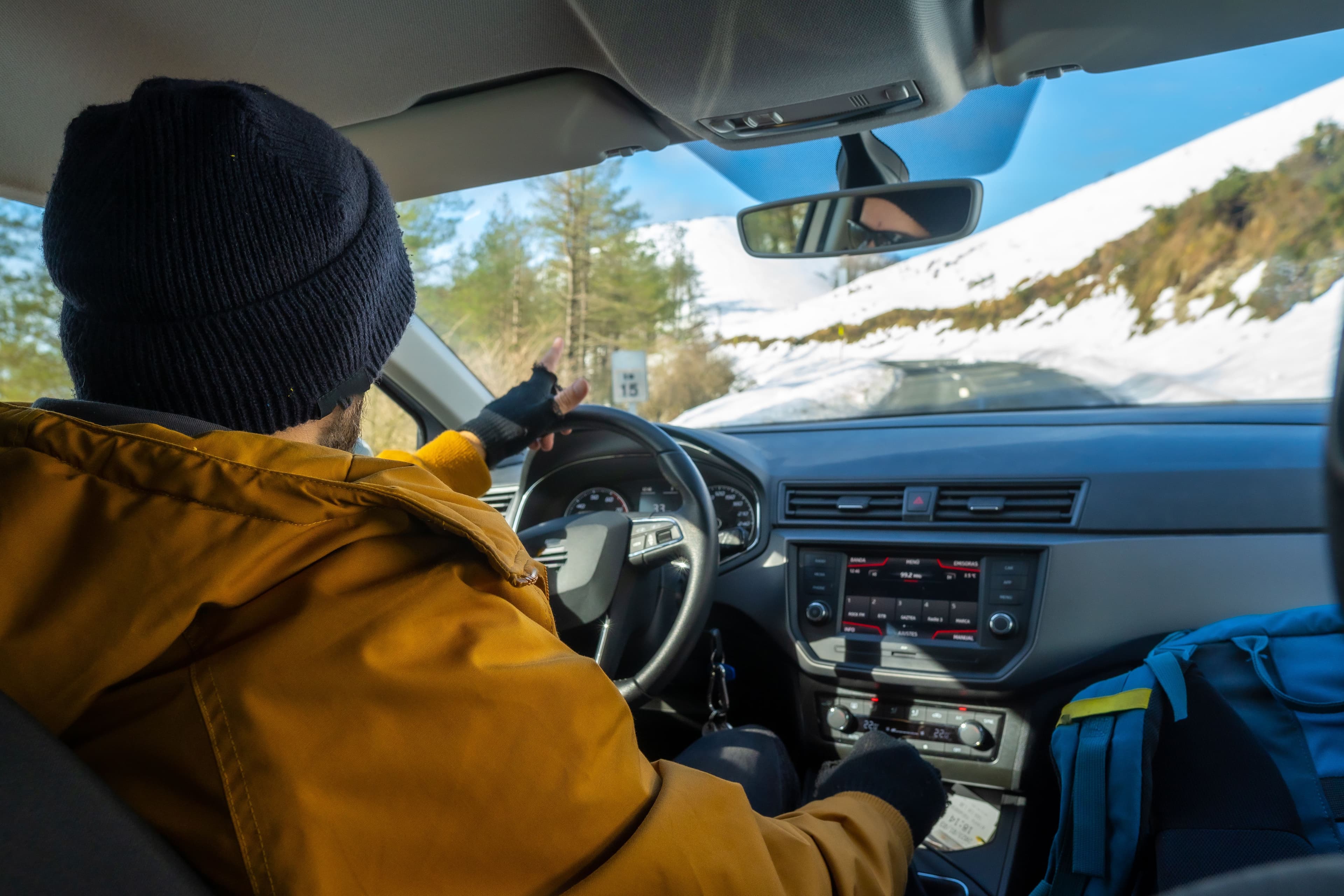 A man driving down a narrow, snowy road in winter, watching the road carefully for hazards such as black ice.