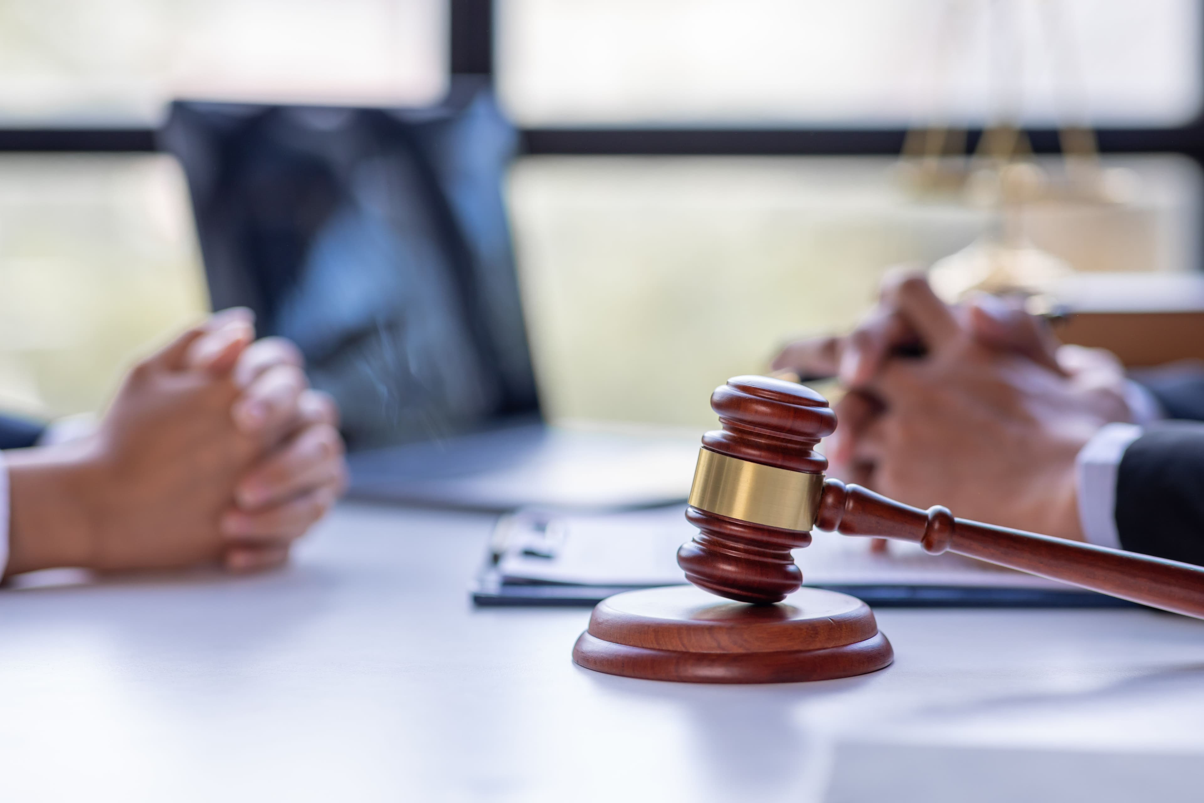Folded hands of a client and hired personal injury lawyer sitting across from each other, with a gavel in the foreground.