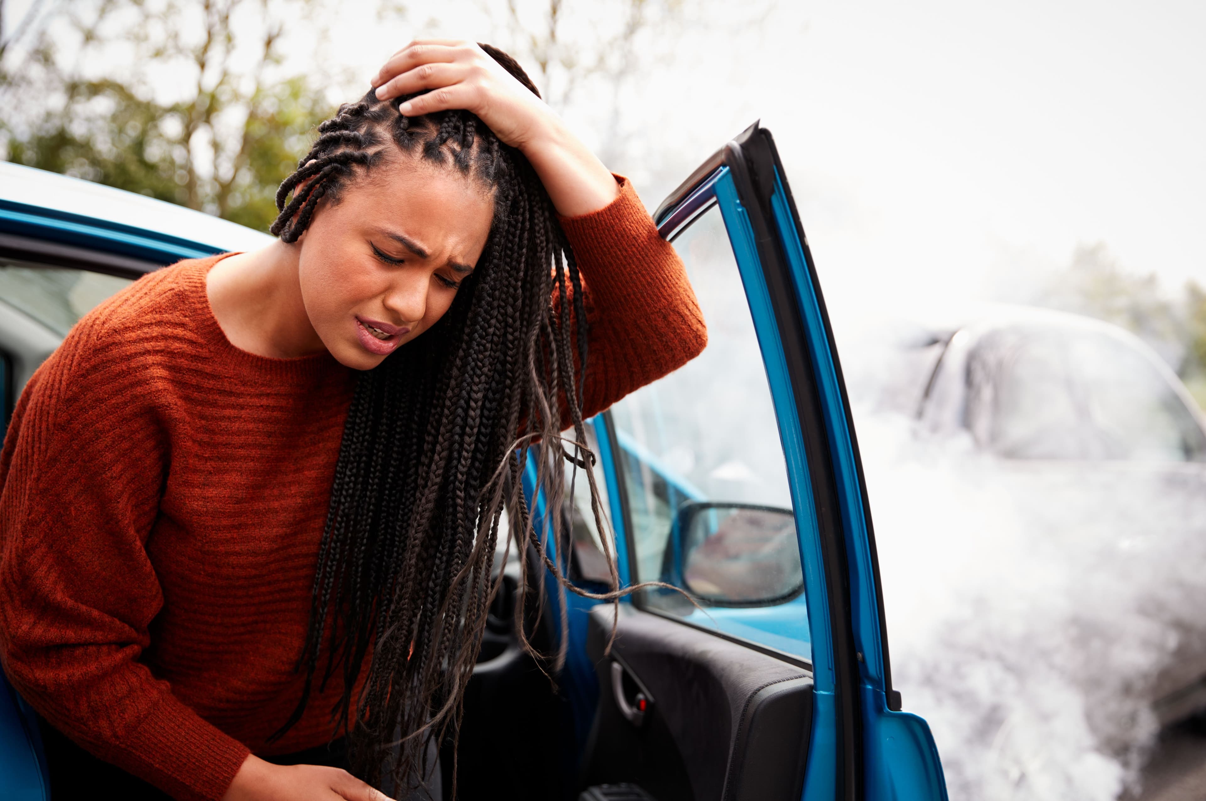 Female driver getting out of her car and holding her head after experiencing pain and possible injuries suffered in a car accident.