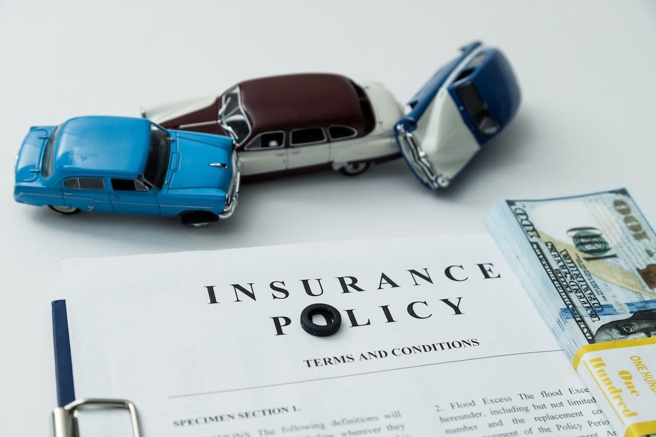 A stack of bills, three miniature cars, and an insurance policy, illustrating Oregon automobile insurance requirements