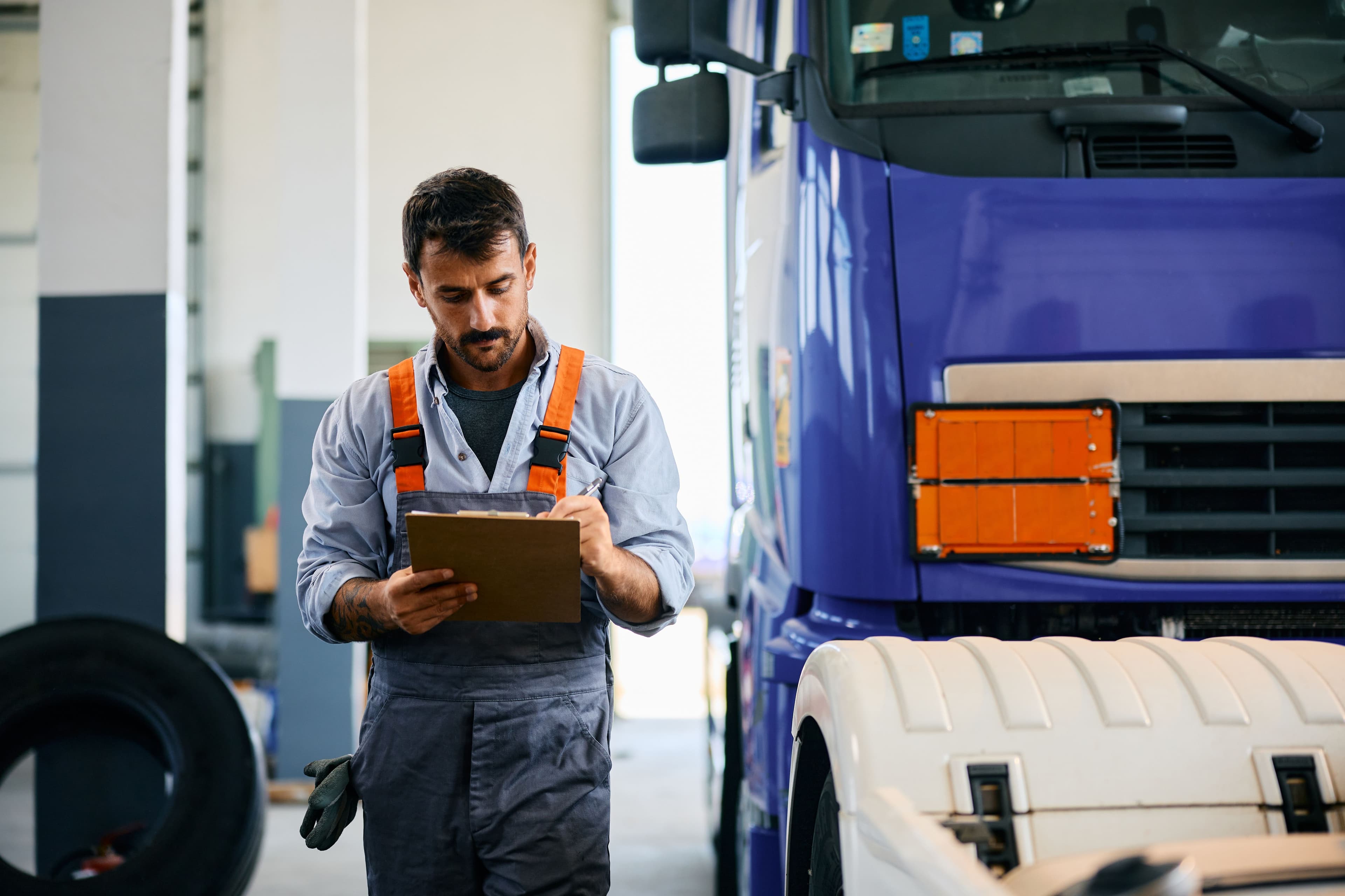 A man checking a clipboard during truck maintenance, an easily overlooked aspect of who is liable in a truck accident.
